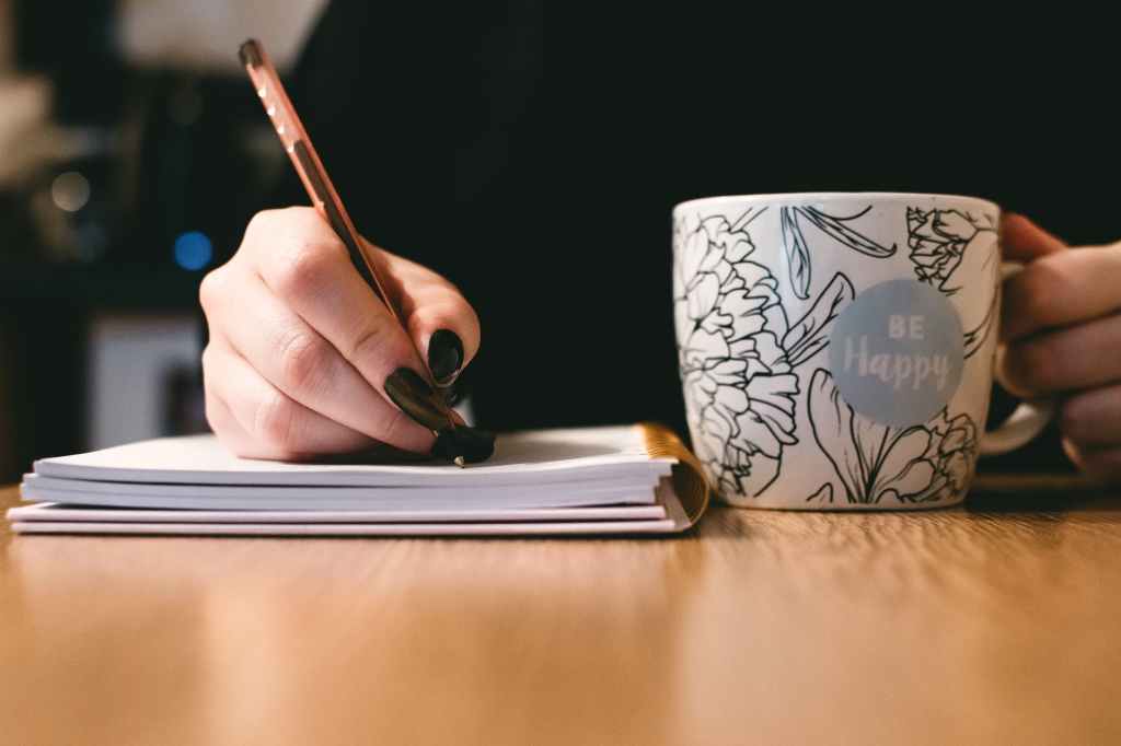 Image showing a person writing over a notebook with a cup of coffee. 